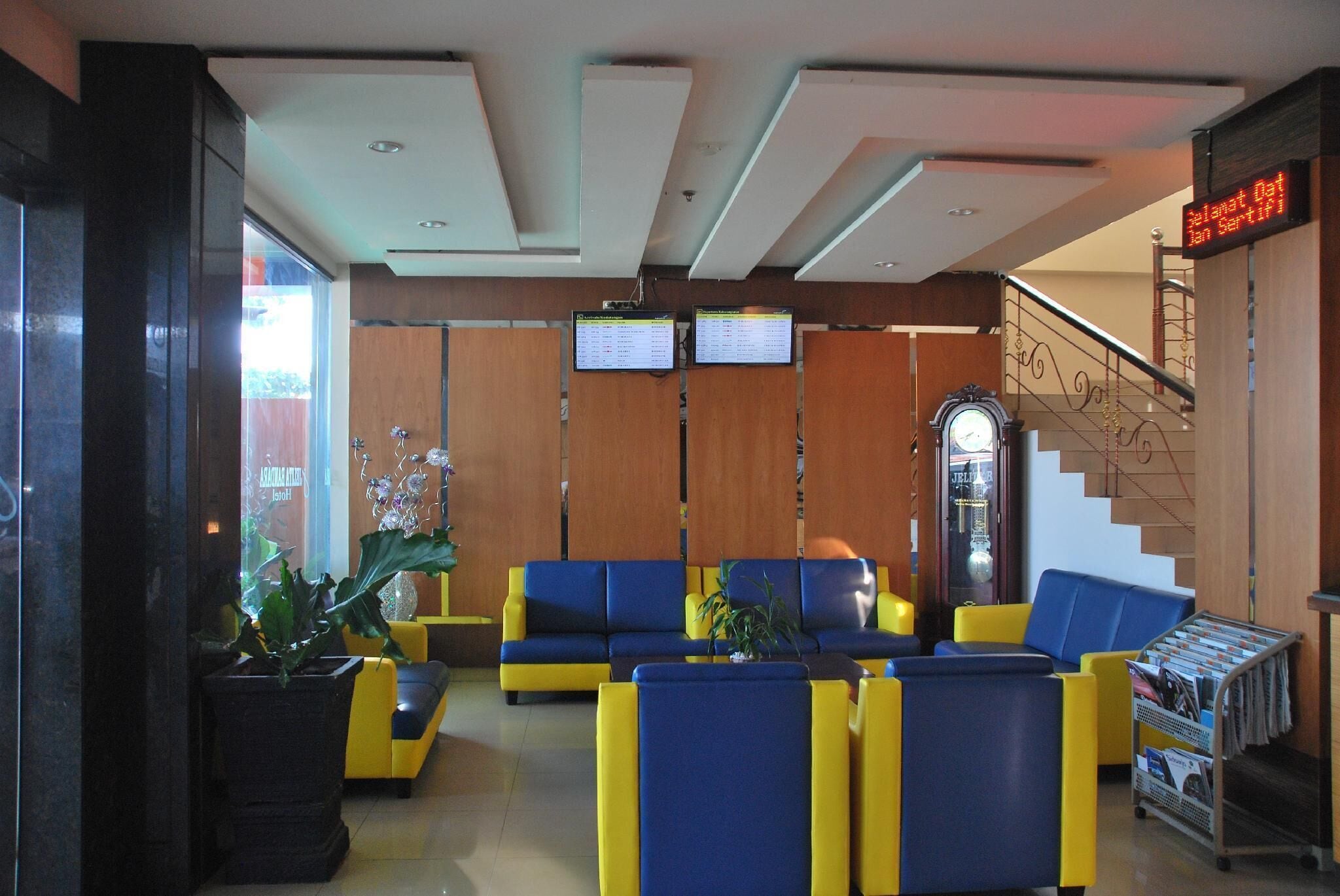 A lobby with yellow and blue seating, a digital display, and a staircase.