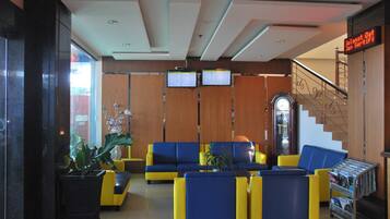 A lobby with yellow and blue seating, a digital display, and a staircase.