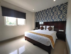 A hotel room with a large bed, a headboard with a patterned design, a bedside table, and a window with a blackout curtain.