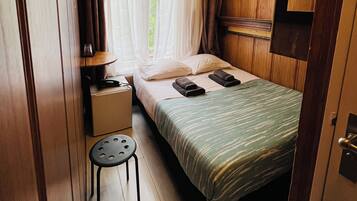 Un dormitorio pequeño con una cama individual, una mesita de noche, una silla y una ventana con cortinas.