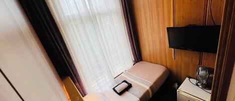 Una habitación de hotel pequeña con cama, escritorio, televisor y un mueble bajo.