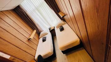 A compact cabin with two beds, a wooden floor, and a window with sheer curtains.