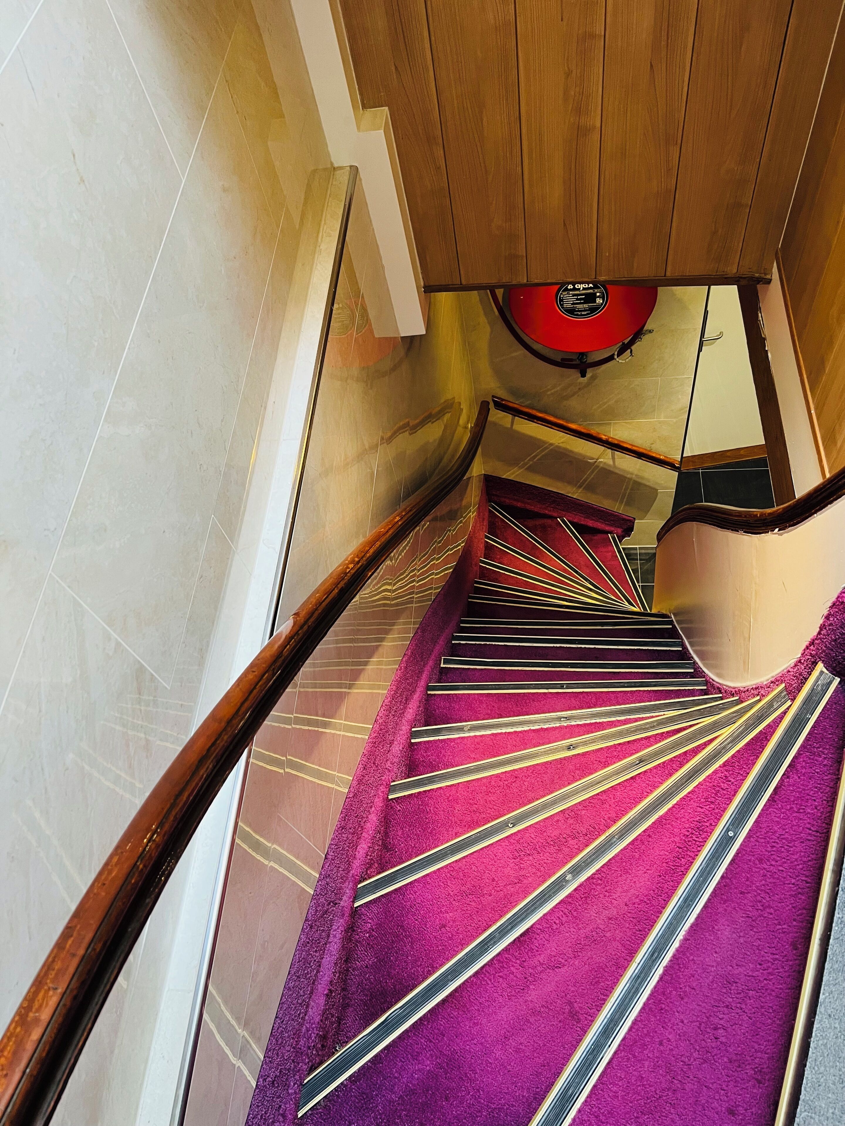 A staircase with a wooden handrail and a purple carpet.