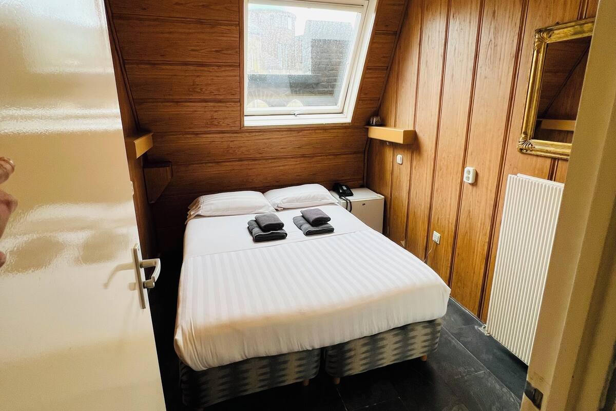 Un dormitorio pequeño con una cama individual, una mesita de noche, un tablero lateral, una ventana con vistas y paneles de madera.