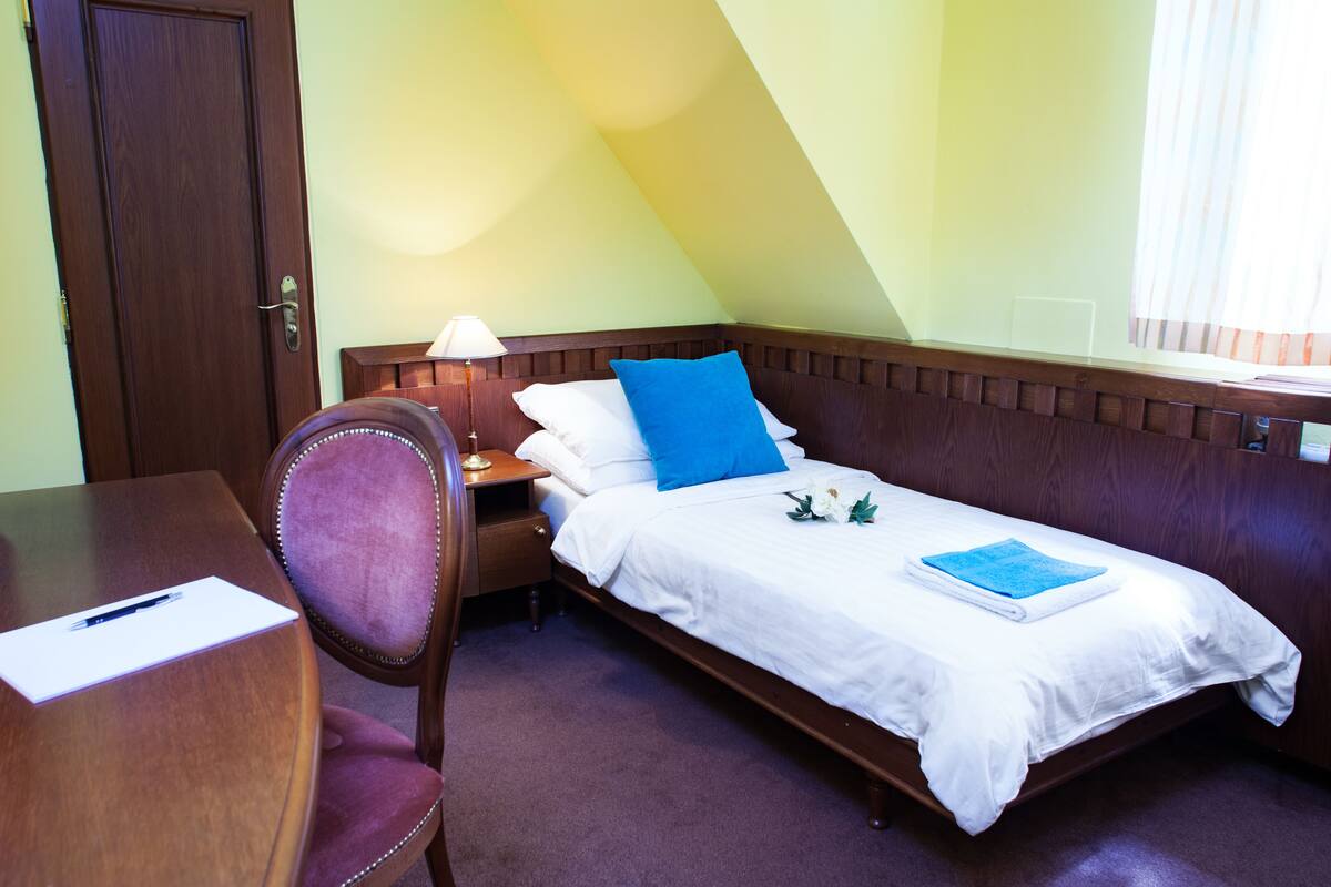A single bed with a wooden headboard, a desk with a chair, and a lamp.