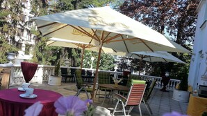 An outdoor patio area with tables and chairs under umbrellas, surrounded by greenery and trees. - Hotel Villa Ostrava (Ostrava)
