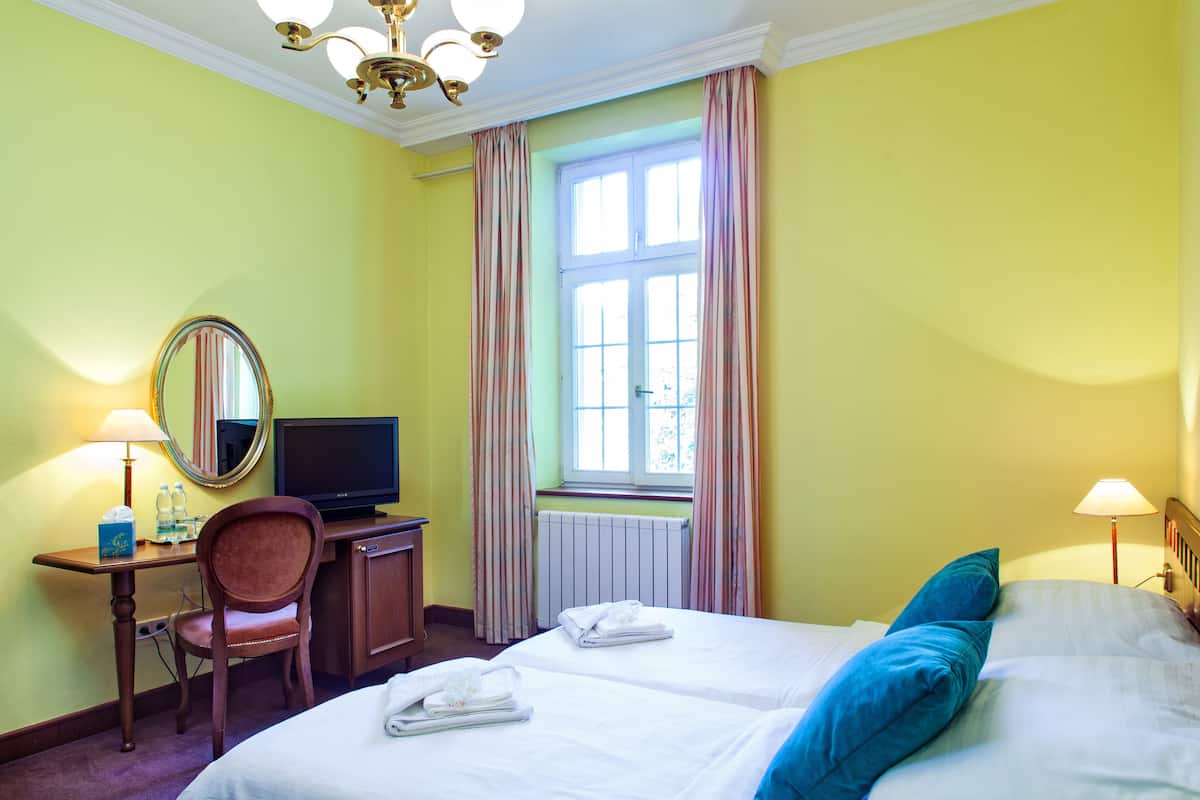 A hotel room with two beds, a desk with a television, a chair, and a window with curtains.