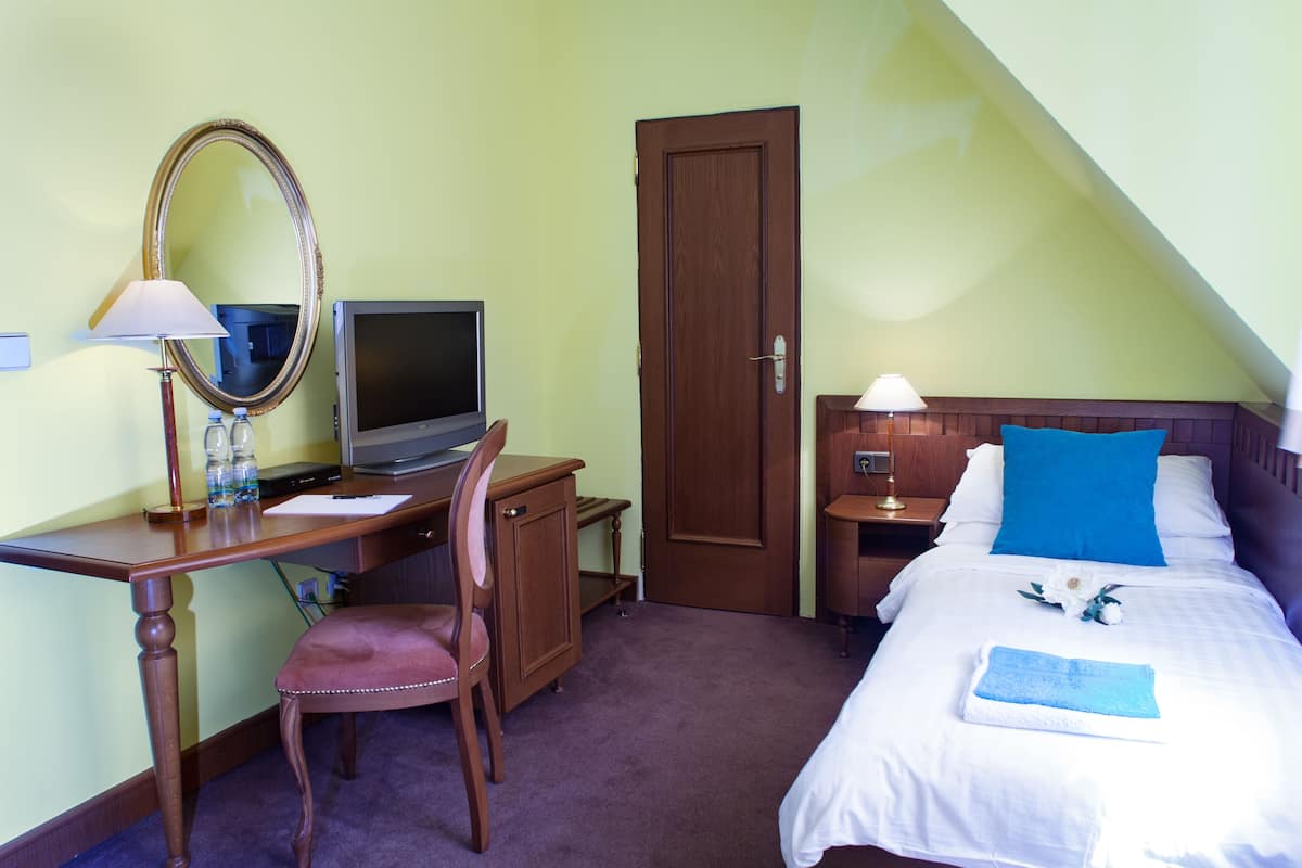 A hotel room with a desk, chair, television, and a bed with a blue pillow and white bedding.