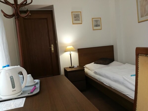 A hotel room with a bed, bedside lamp, wooden nightstand, and a table with a kettle and cups. - Hotel Villa Ostrava (Ostrava)