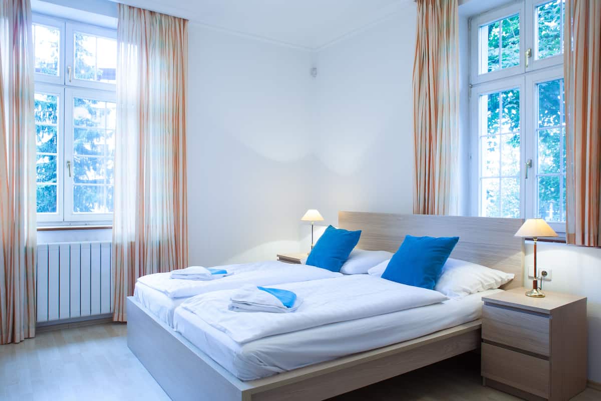 A hotel room with a large bed, two bedside tables, and a window with curtains.