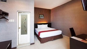 Habitación de hotel con cama, escritorio, silla, puerta con panel de vidrio decorativo y televisor montado en la pared.