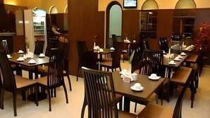 Un restaurante con varias mesas y sillas, un televisor en la pared y una estantería al fondo.