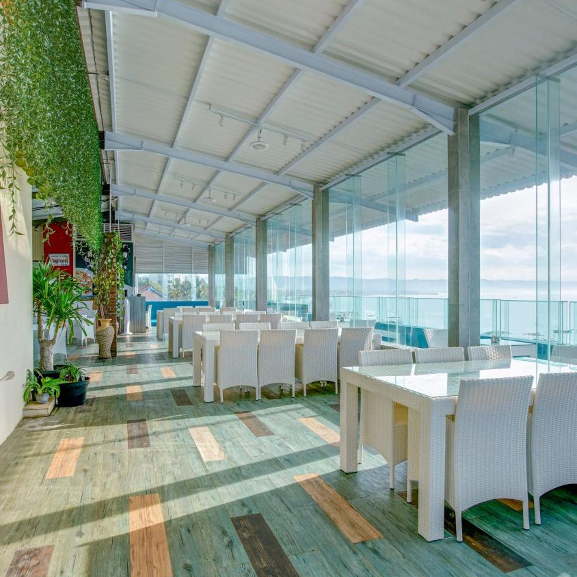 A spacious indoor area with white wicker furniture, large windows, and a view of the sky.