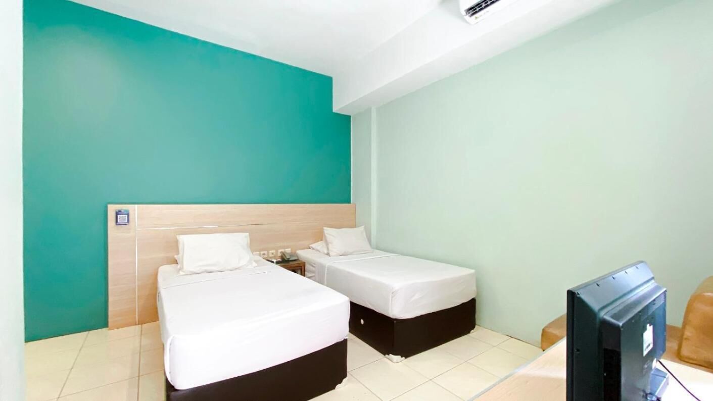 A hotel room with two single beds, a wooden headboard, a television, and a small table.