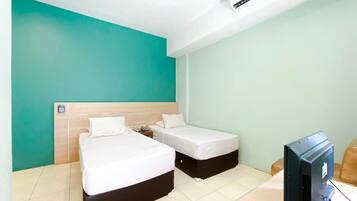 A hotel room with two single beds, a wooden headboard, a television, and a small table.