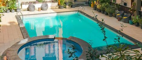 Piscina com hidromassagem circular, rodeada por plantas em vasos e área de estar ao ar livre.