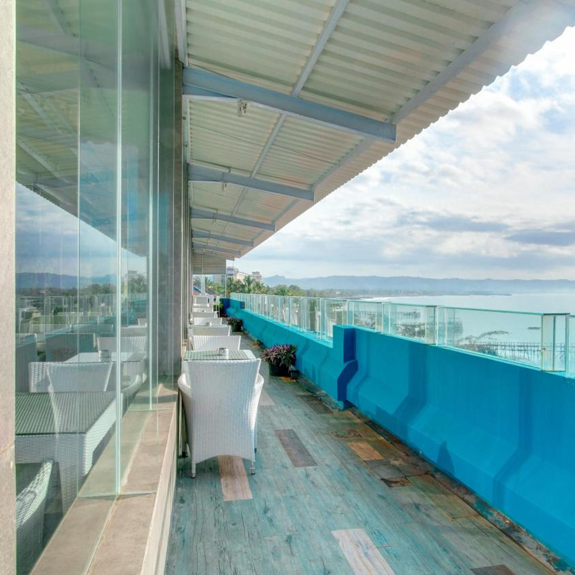 A covered outdoor balcony with seating and a view of the sea.