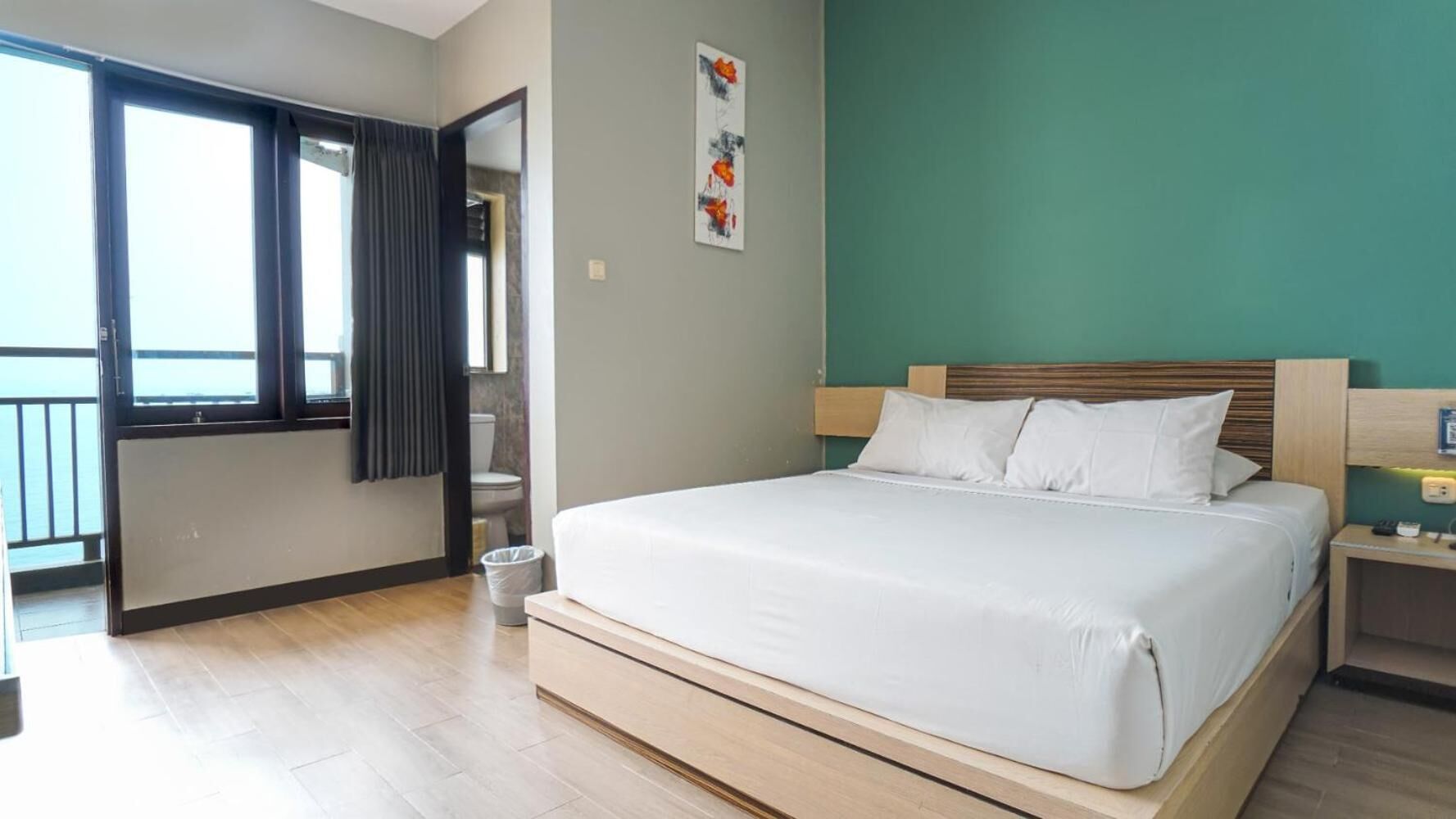 A hotel room with a large bed, a wooden headboard, a nightstand with a lamp, and a view through an open door to a balcony.