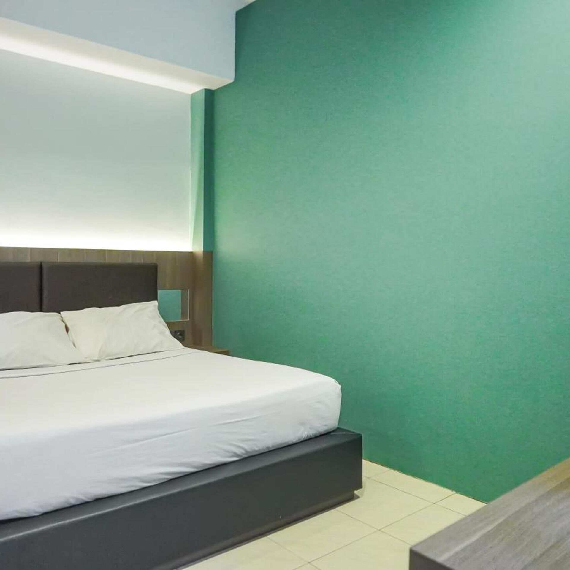 Un letto con biancheria bianca, una testiera scura e una parete verde.