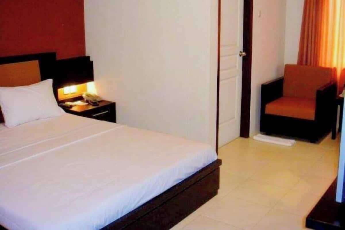A hotel room with a bed, bedside table, chair, and a door.