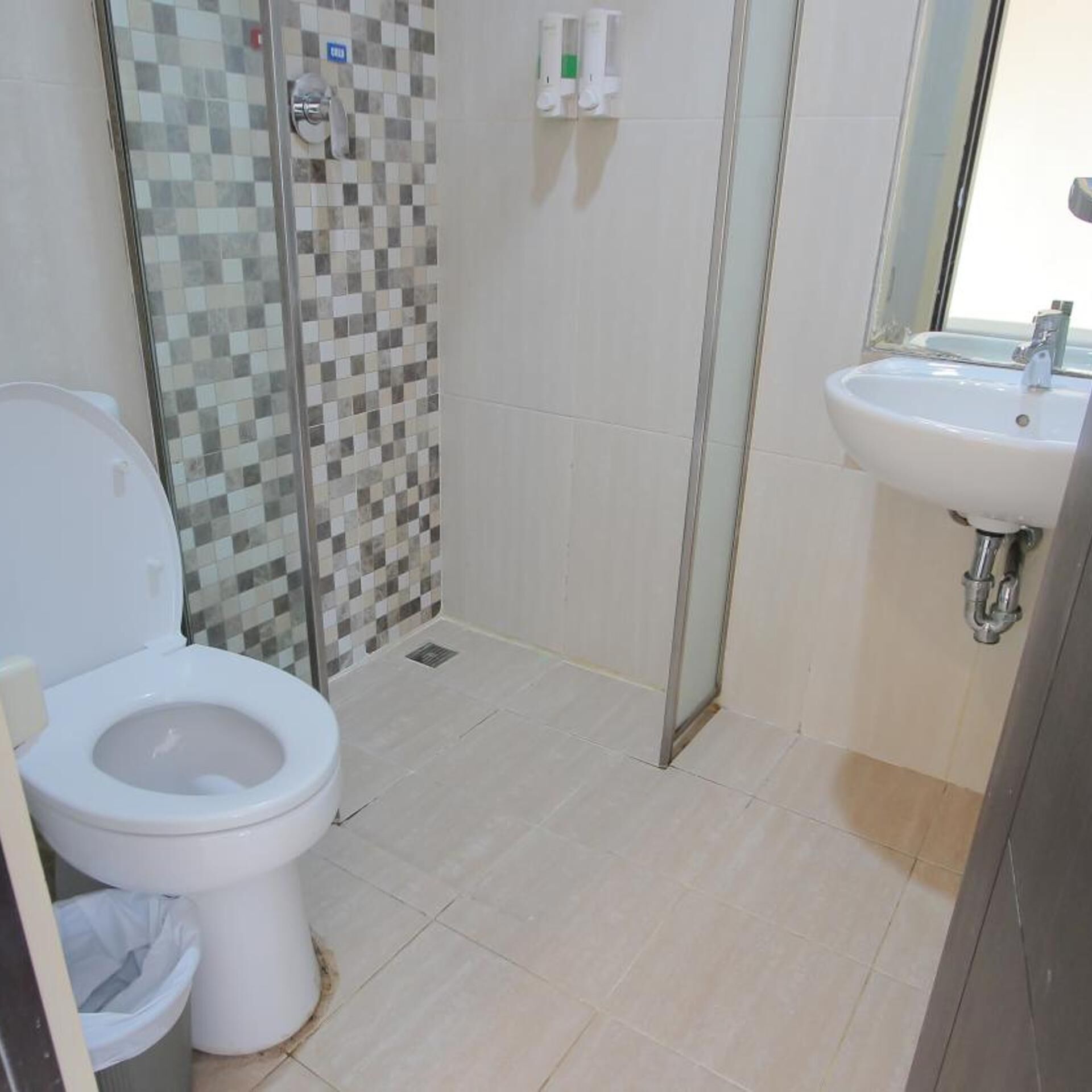 Un baño con inodoro, ducha con pared de azulejos y lavamanos con espejo.