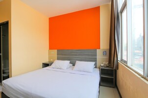 Una habitación de hotel con una cama, una mesita de noche, un ventanal con cortinas y una pared de acento naranja brillante.