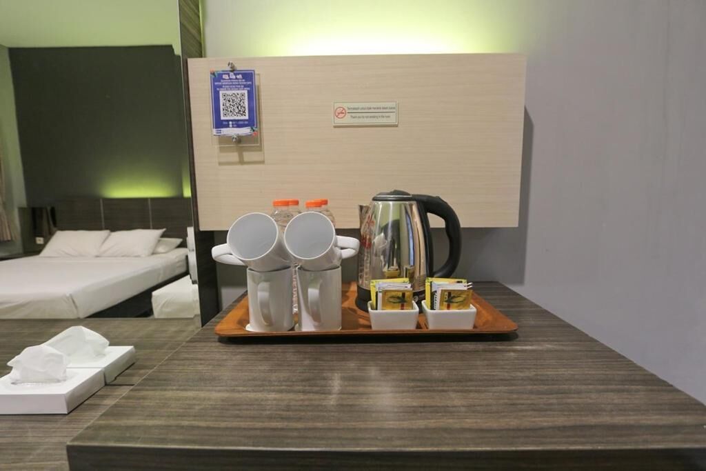 Habitación de hotel con una cama, un carrito con tazas, un hervidor y una mesita con una caja de pañuelos.
