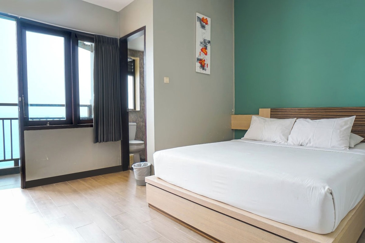 Habitación de hotel con cama, mesita de noche, una obra de arte colgada en la pared y vistas a través de una puerta abierta.