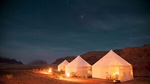 Tres tiendas de campaña en un desierto bajo un cielo estrellado.