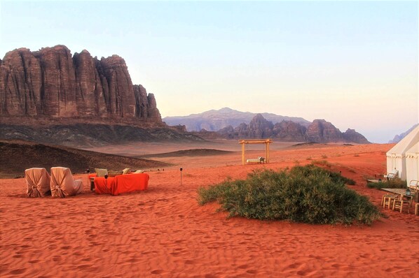 A desert landscape with a white tent and a small structure with a table and chairs.