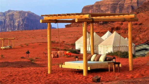 Un campamento en el desierto con una hamaca de madera, tiendas de campaña y vistas a formaciones rocosas rojas.