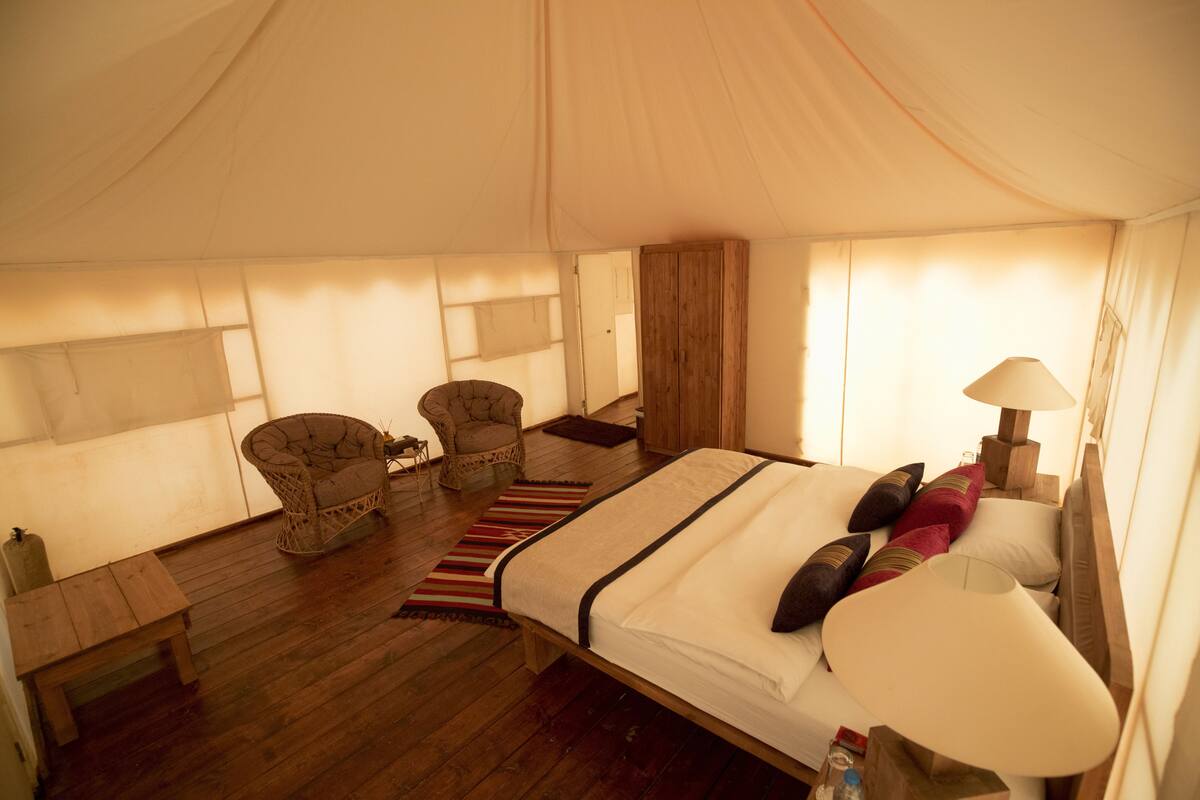 A tented room with a bed, a chair, a table, and a lamp.