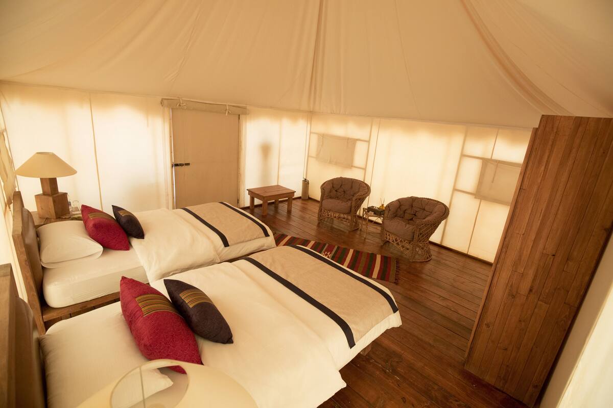A tented accommodation with two beds, a small table, and two chairs.