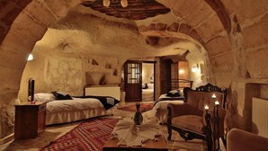 A cozy, rustic bedroom with a stone archway, a bed with a white duvet, a wooden chair, and a small table with a vase. - Heaven Cave House (Ürgüp)