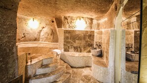 A luxurious spa with a stone interior, a curved bathtub, and a tiled floor. - Heaven Cave House (Ürgüp)