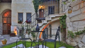 A courtyard with a stone wall, a staircase, and outdoor seating with metal chairs and a table. - Heaven Cave House (Ürgüp)