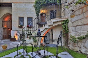 Un patio con muro de piedra, una escalera y mobiliario exterior con sillas de metal y una mesa.