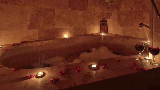 A hot tub with rose petals and candles, surrounded by stone walls. - Heaven Cave House (Ürgüp)