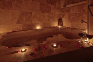 A hot tub with rose petals and candles, surrounded by stone walls. - Heaven Cave House (Ürgüp)
