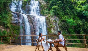 A couple dining at a table with a view of a waterfall.
