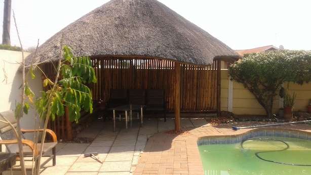 A thatched-roof outdoor seating area with a pool. - Comfort Palace Guest House Francistown (Francistown)