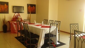 A dining area with a round table, metal chairs, and a TV on the wall. - Comfort Palace Guest House Francistown (Francistown)