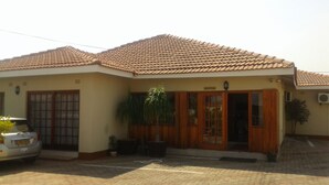 A building with a tiled roof, a reception area, and a car parked in front. - Comfort Palace Guest House Francistown (Francistown)