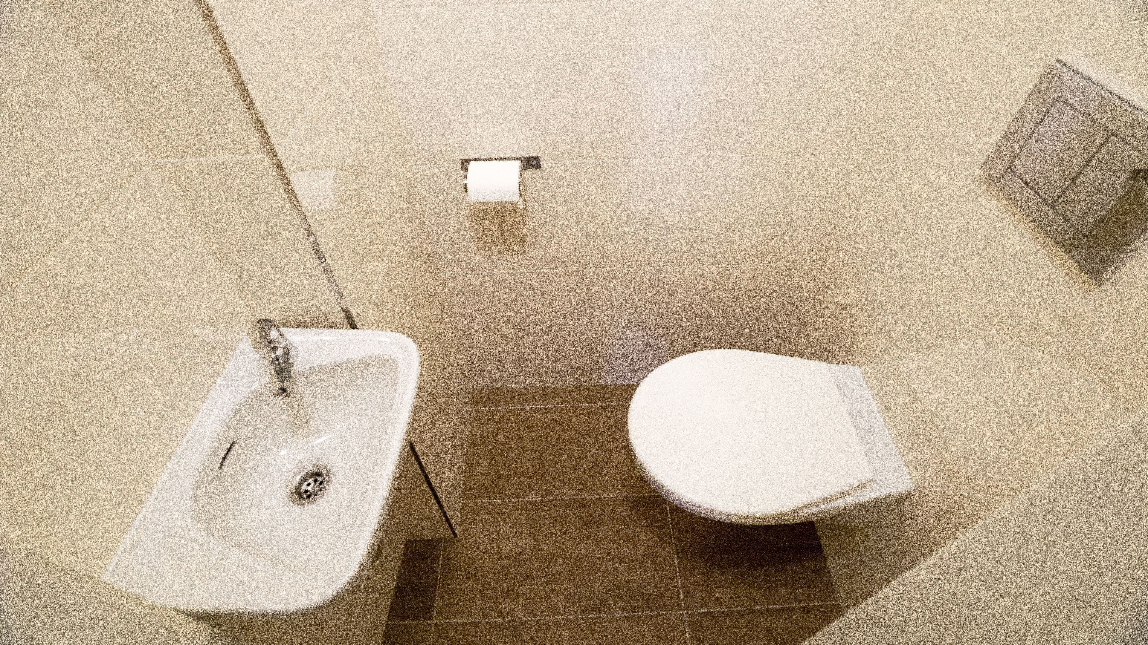 A small bathroom with a sink and toilet, tiled floor, and a toilet paper holder on the wall.