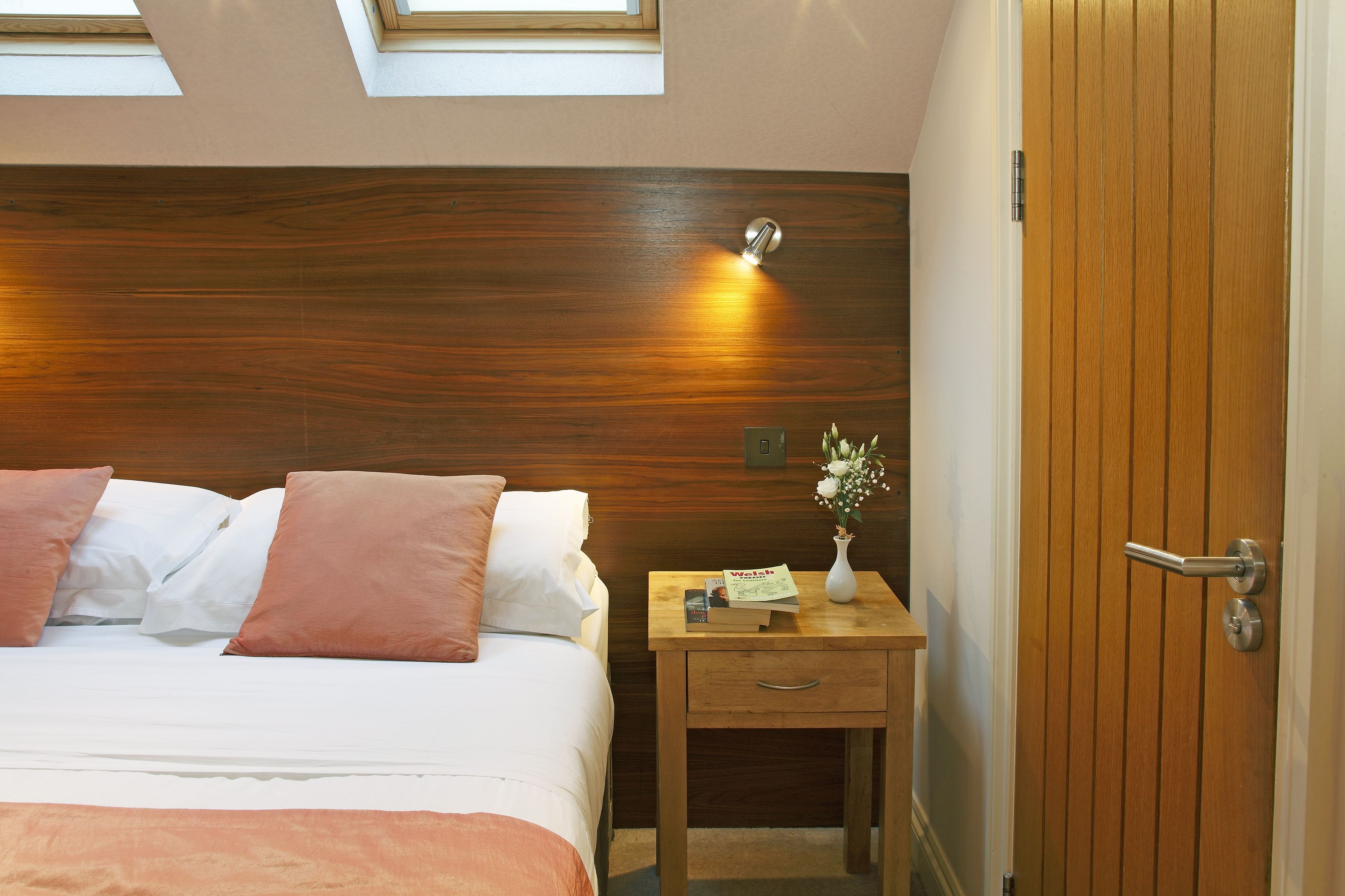 A bedroom with a wooden headboard, a bedside table with a book and a vase, and a door with a handle.