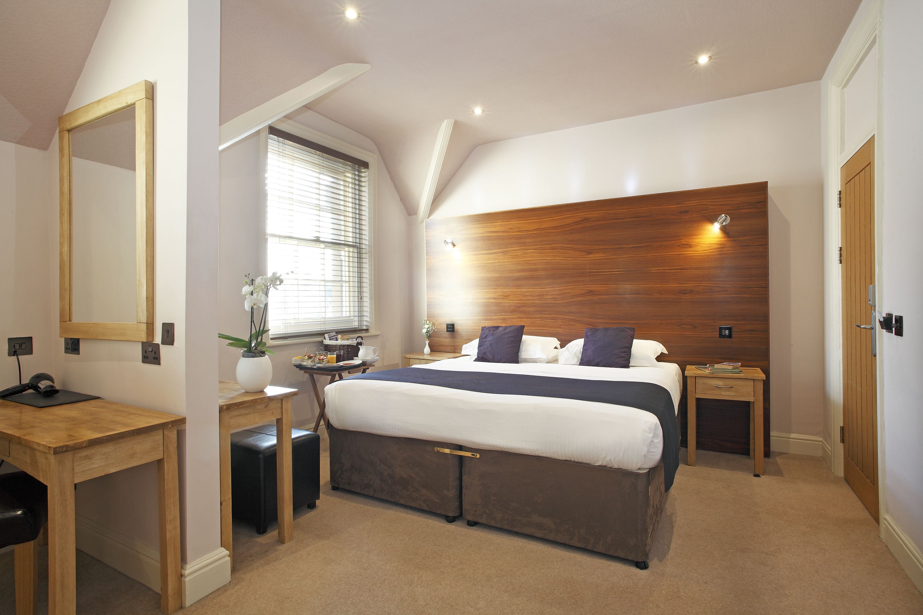 A bedroom with a large bed, a wooden headboard, a desk, and a mirror.