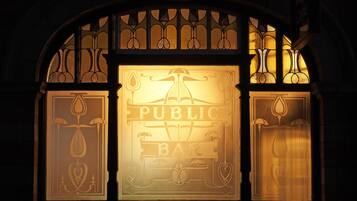 Un letrero enmarco con el texto 'PUBLIC BAR', situado en un interior oscuro con decoración de hierro forjado.