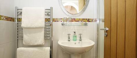 A bathroom with a white sink, a towel rack with three towels, a mirror, and a tiled backsplash.