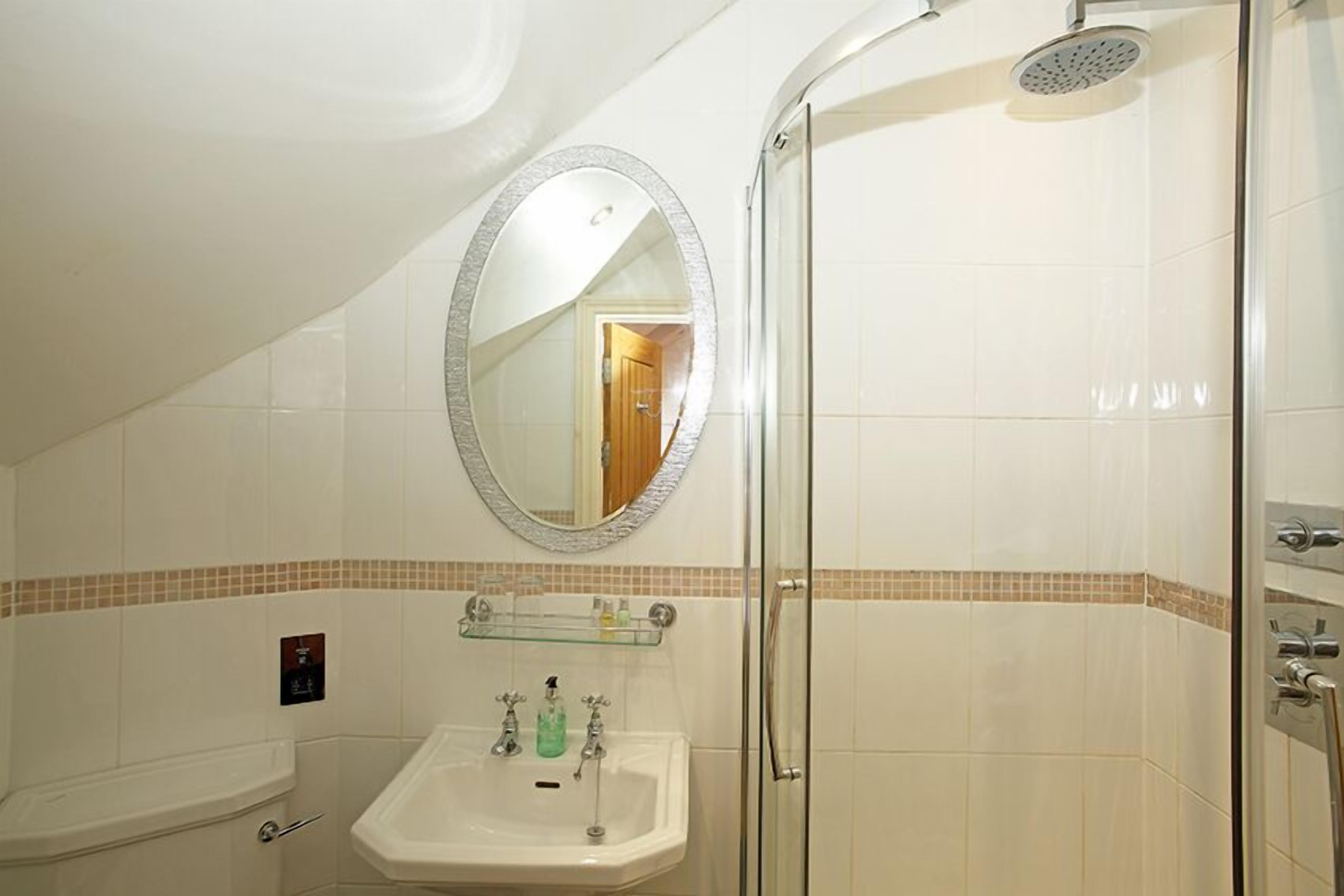 Une salle de bain avec une douche à parois de verre, un lavabo avec un miroir au-dessus et une petite étagère contenant des articles de toilette.