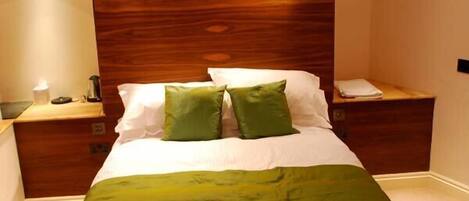 Un dormitorio con cabecera de madera, dos mesitas de noche, cama con ropa de cama blanca y almohadas verdes, y una manta verde.